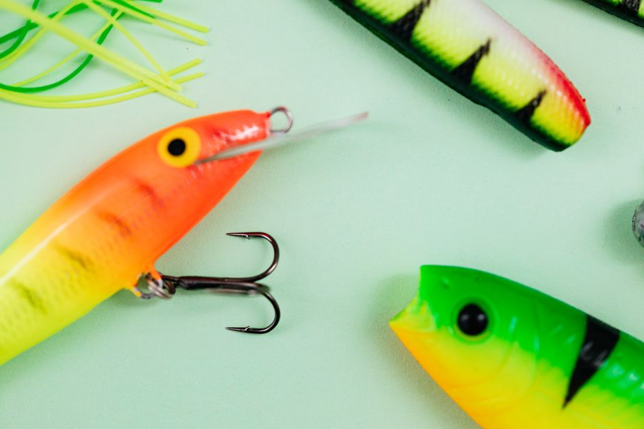 Vibrant fishing lures featuring hooks on a pale green background, ideal for fishing enthusiasts.